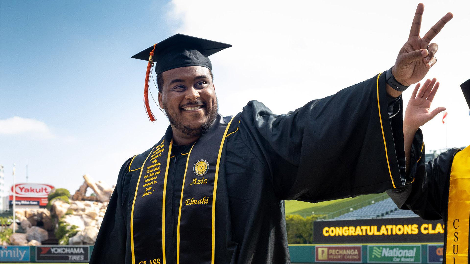 Male graduate gives peace sign with two fingers to Commencement crowd