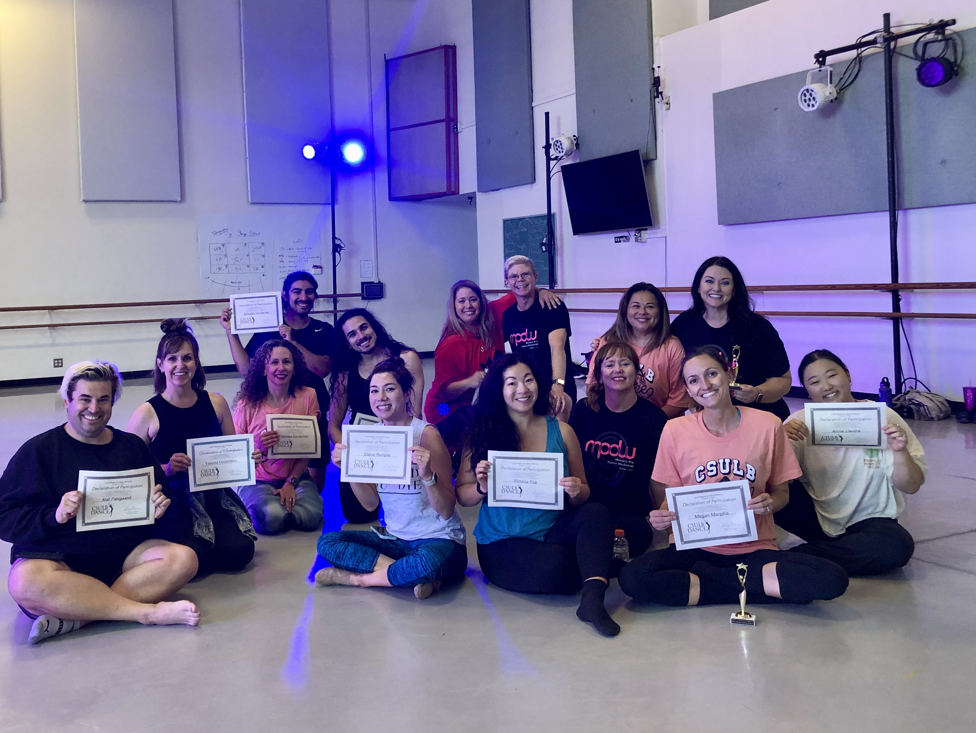 Fourteen dancers sit and display their awards.