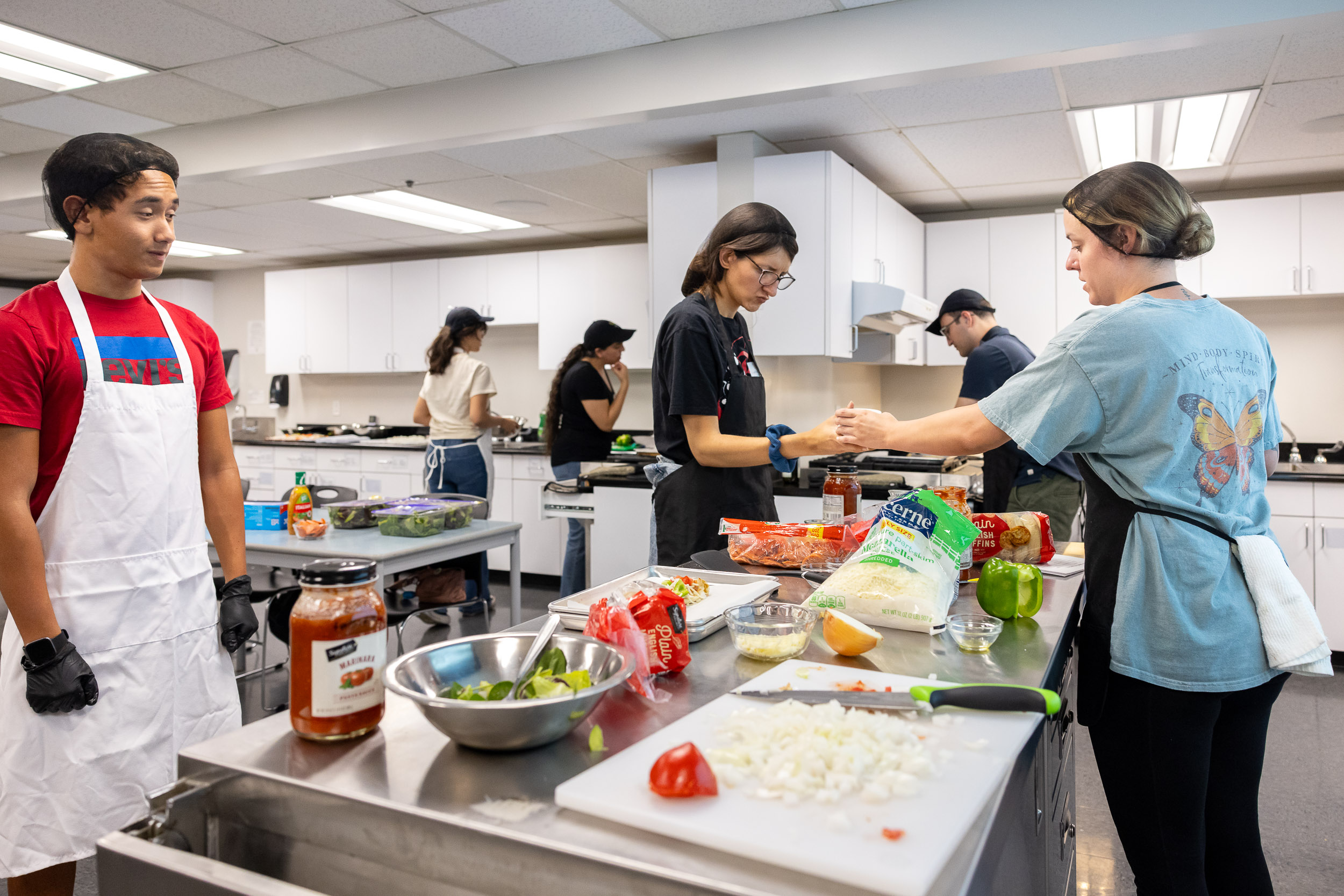 Summer LIFE students work with staff and peer mentors preparing food in a kitchen classroom filled with ingredients and cooking utensils.