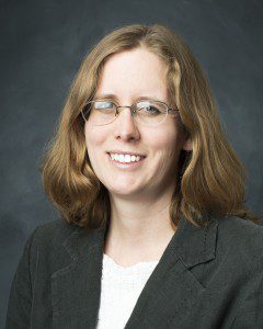 Smiling white woman with medium length light brown wavy hair wearing glasses, a white blouse and black jacket