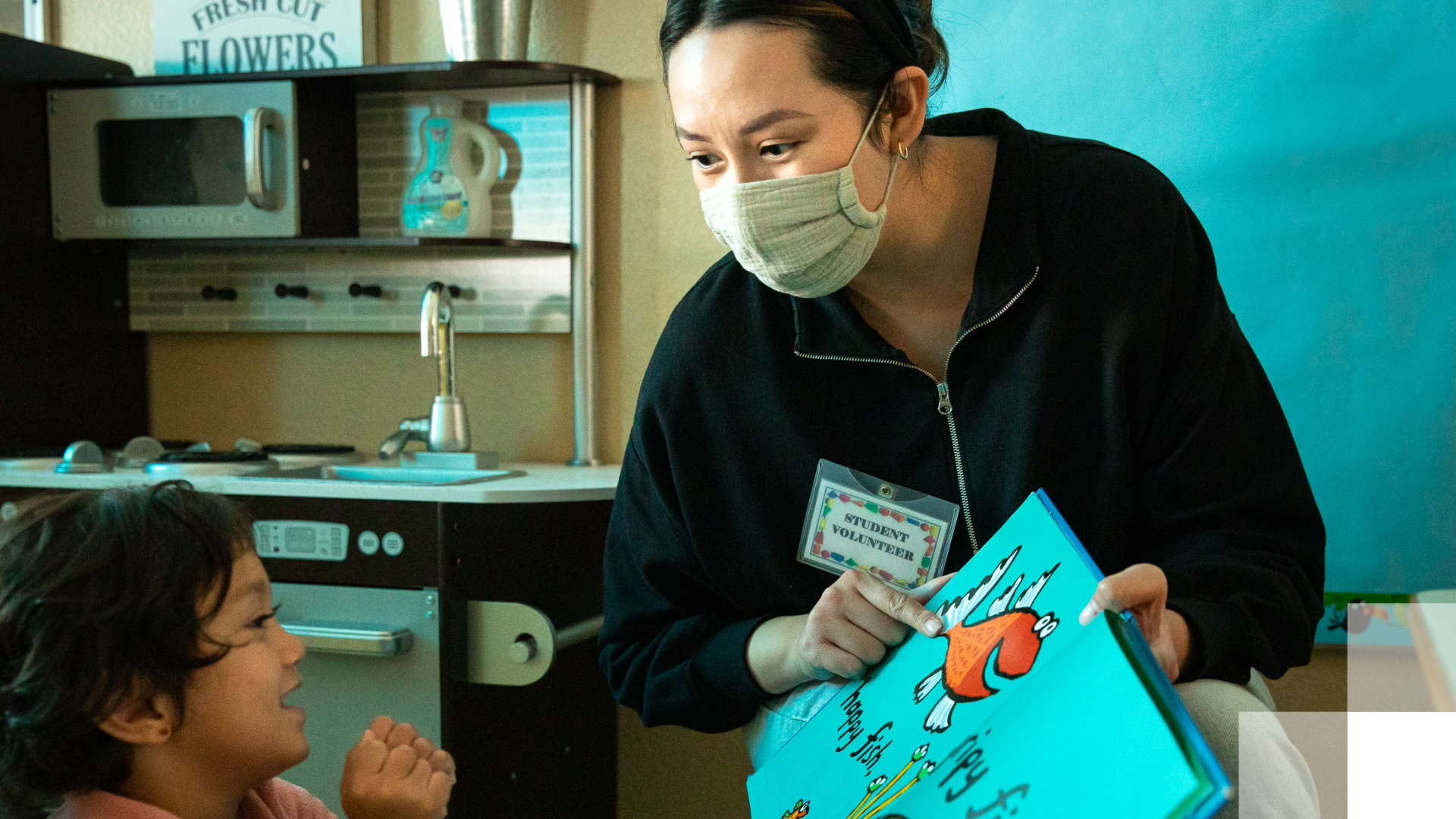 Teacher reads a book with a fish on it to small child.