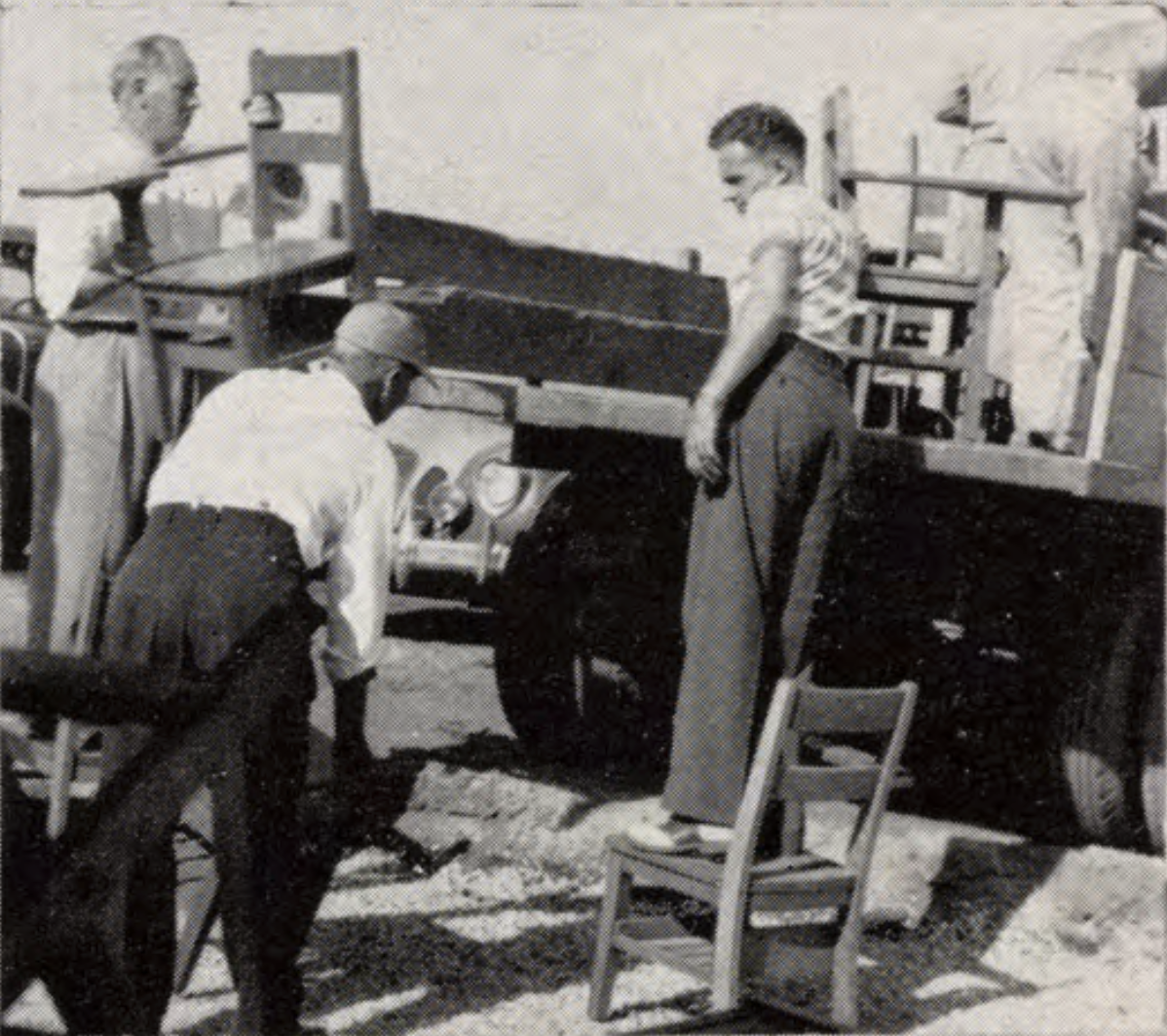 Three men unload chairs from a flatbed truck parked outside.