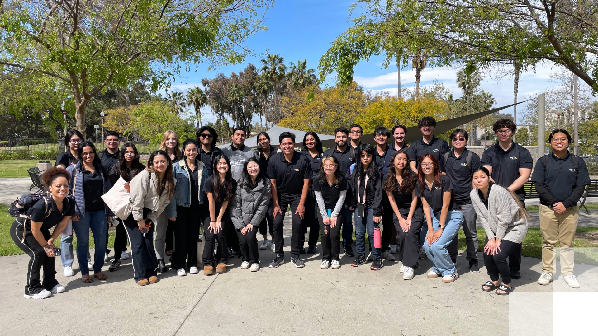 A group of students smile and pose surrounded by trees. 