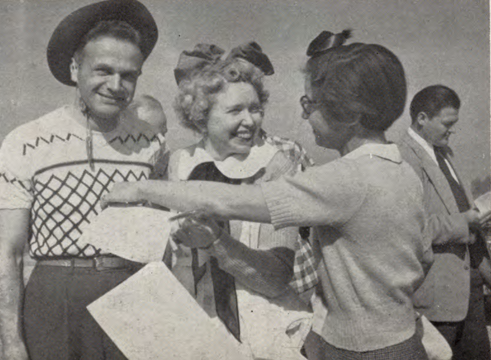 Three people smile and interact, one wearing a cowboy hat, while another holds papers.