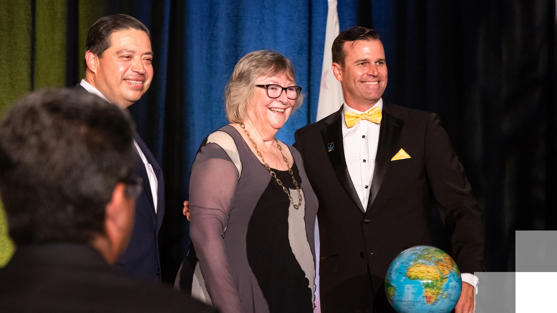 Three adults smile on a stage.