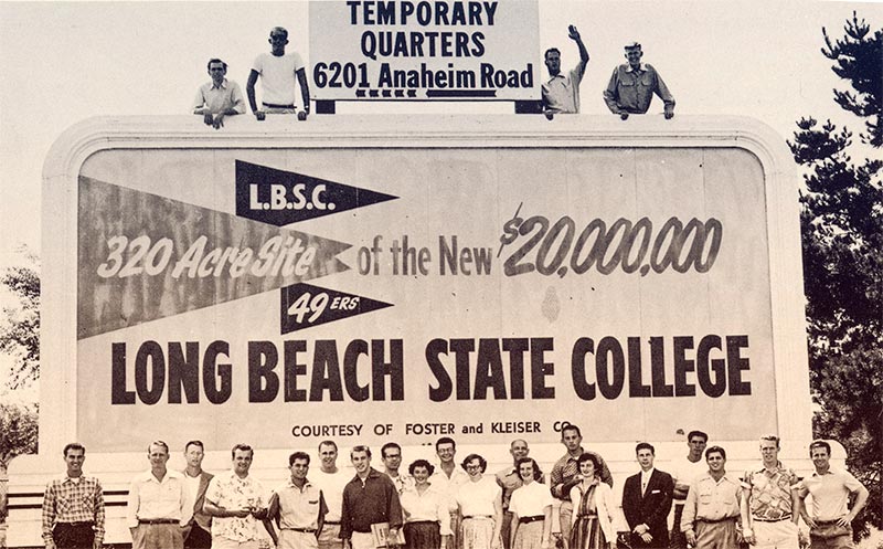 A large group of people stands in front of a billboard advertising the new Long Beach State College site.