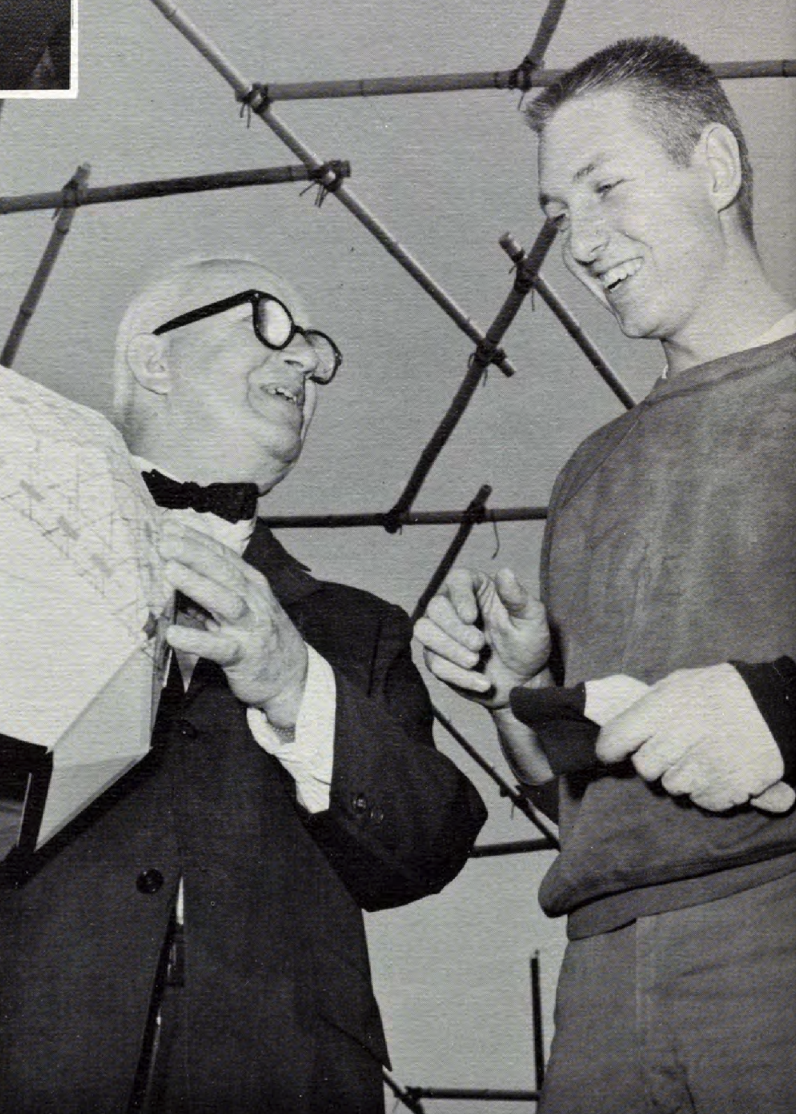 Two people, one holding a geometric object, smile while talking under a structure of connected rods.