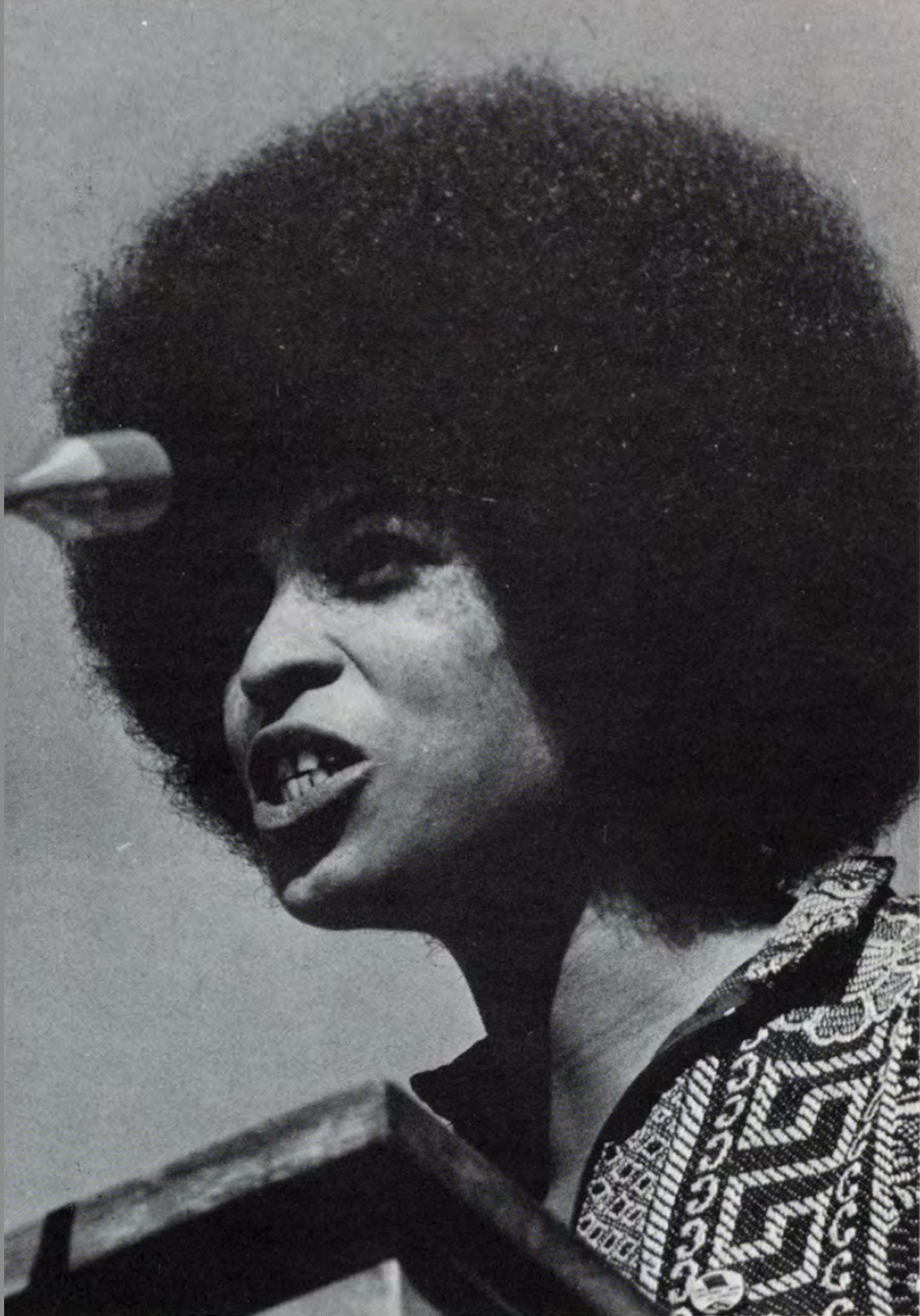 Angela Davis passionately addresses a crowd at a microphone.