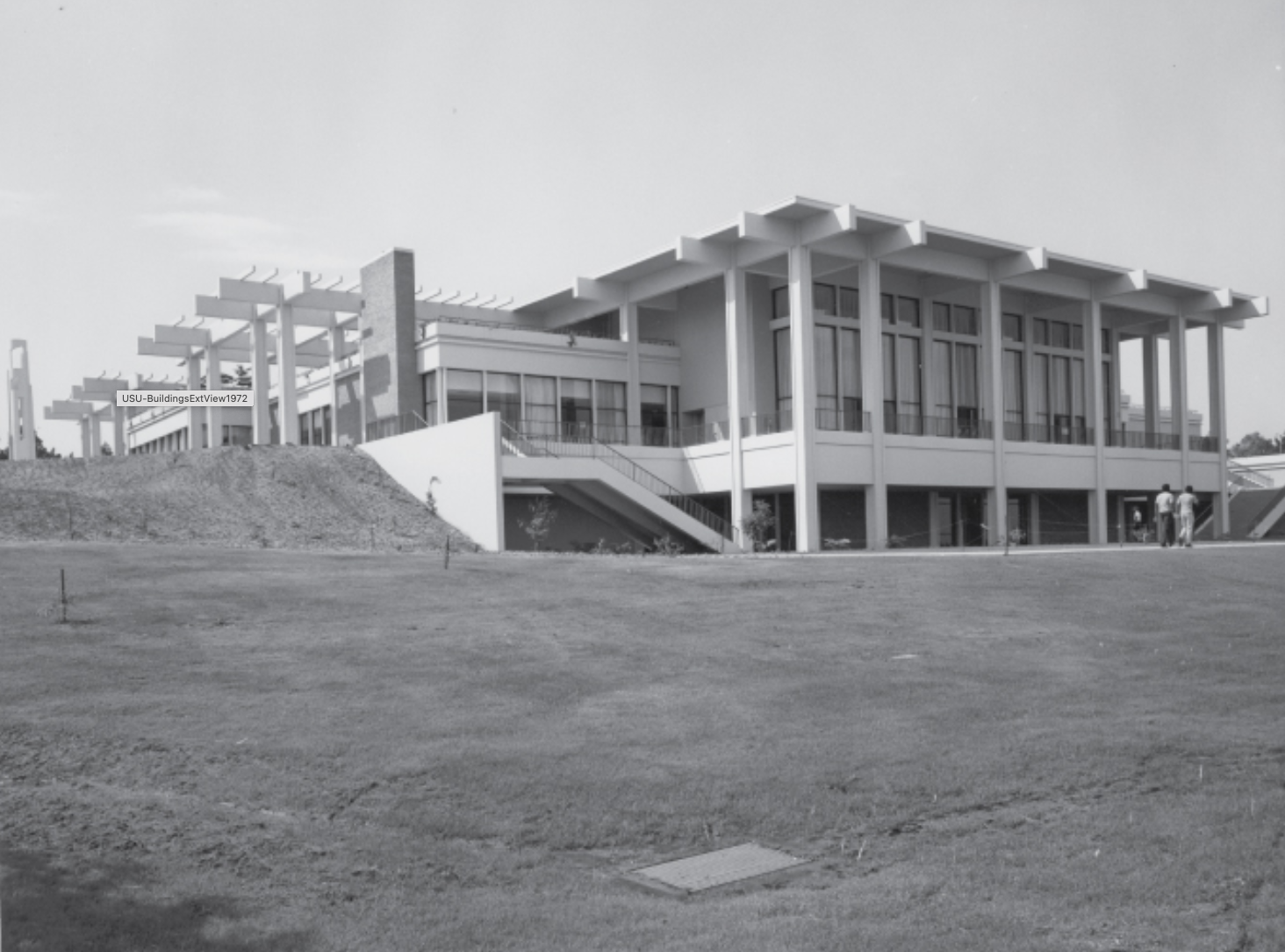 A modern two-story building with large windows and columns stands on a grassy hill.