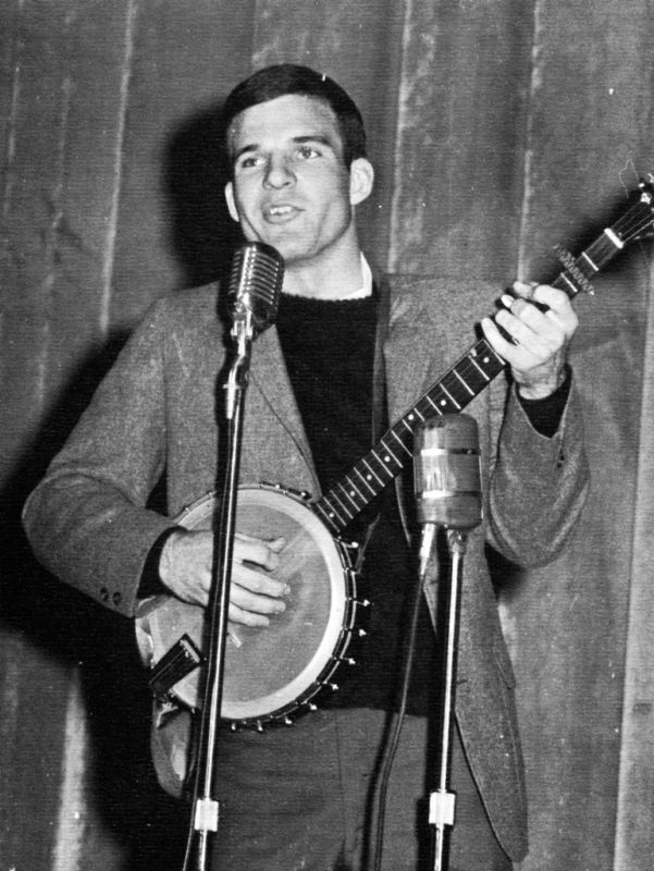 Steve Martin plays the banjo and sings into a microphone on stage.