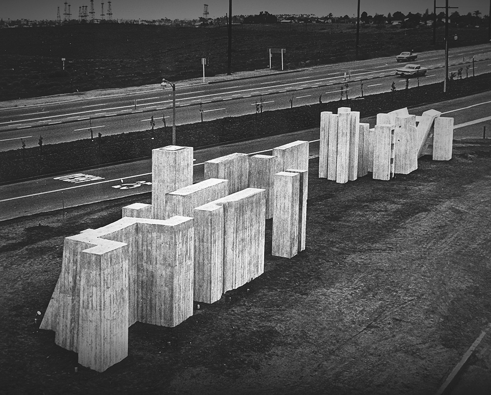 A large concrete sculpture composed of block-like shapes stands near a road.