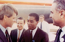 Joseph White stands with other men in suits, including Robert F. Kennedy, converse outside an aircraft.