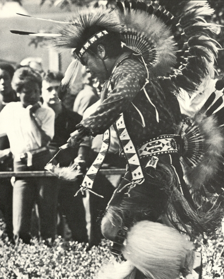 A dancer in traditional Indigenous regalia performs in front of a crowd.