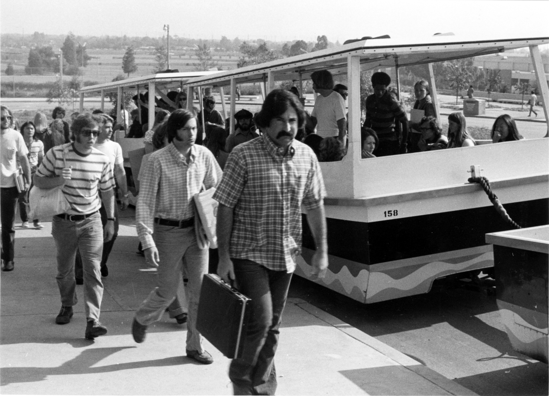 Students exit a campus tram while others board, carrying books and bags.