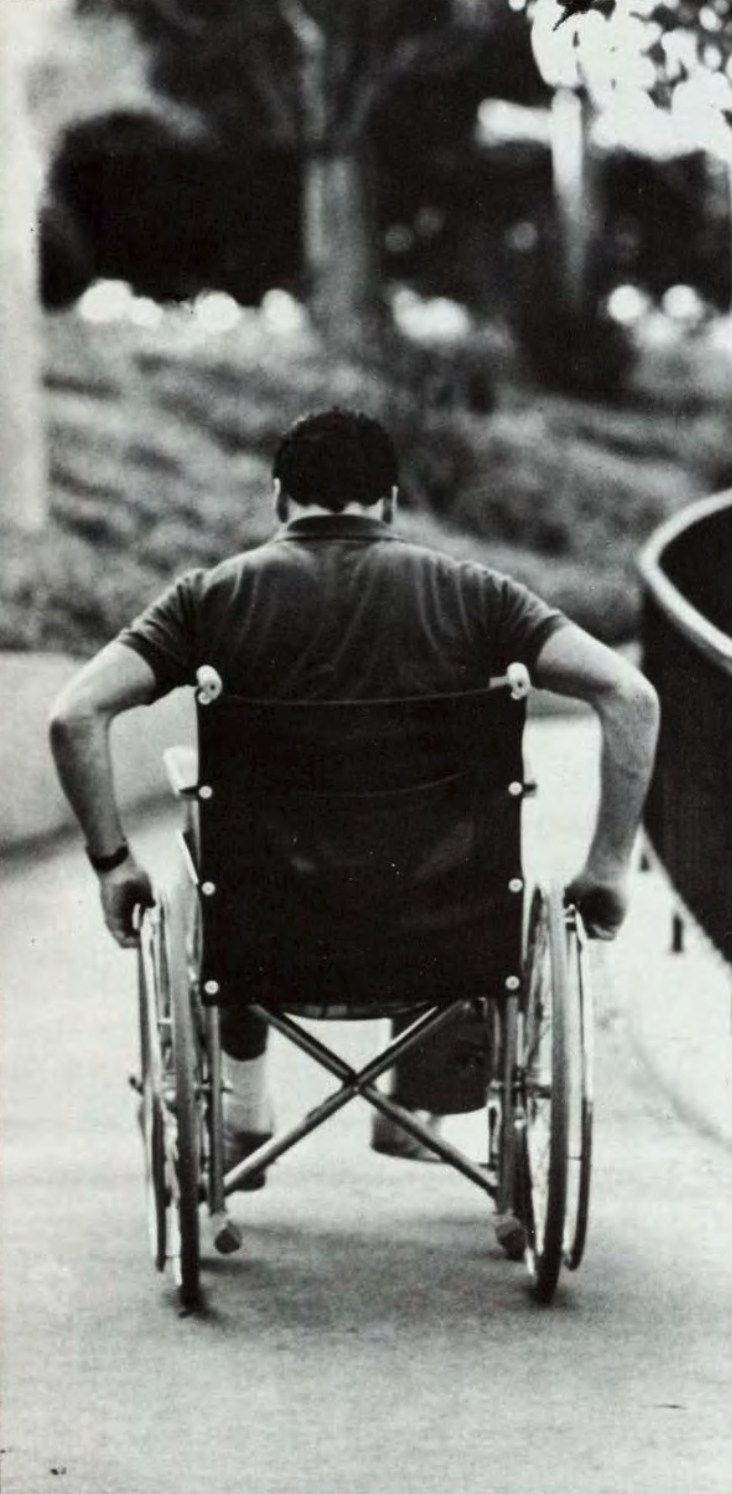 A person pushes a wheelchair along a curved path.