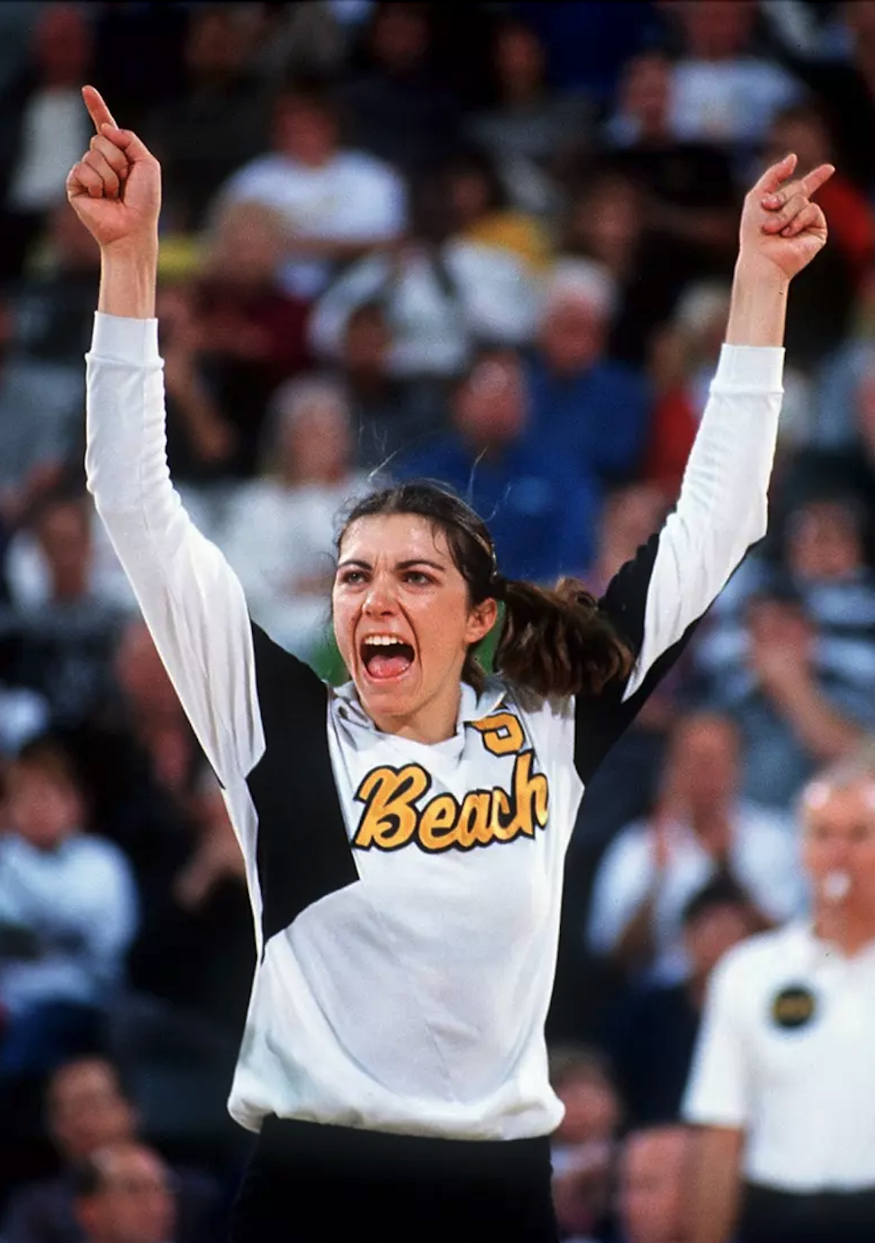 Volleyball player enthusiastically raises both arms, celebrating.