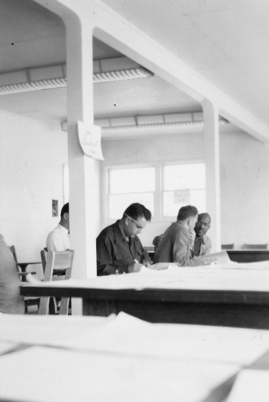 Students sit at tables in a large room and fill out forms.