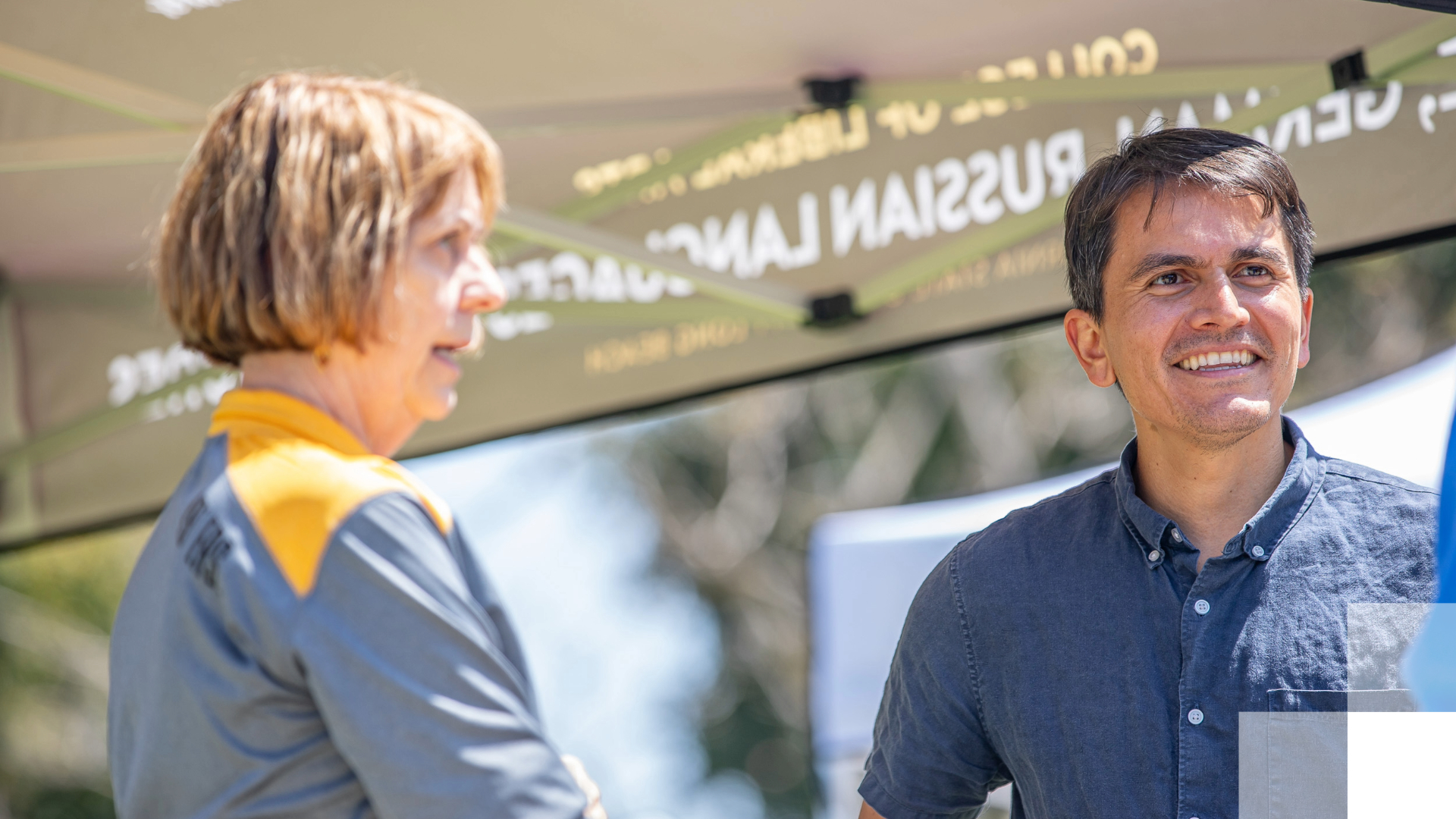 A man and woman stand under a tent that says, "German and Russian Language."