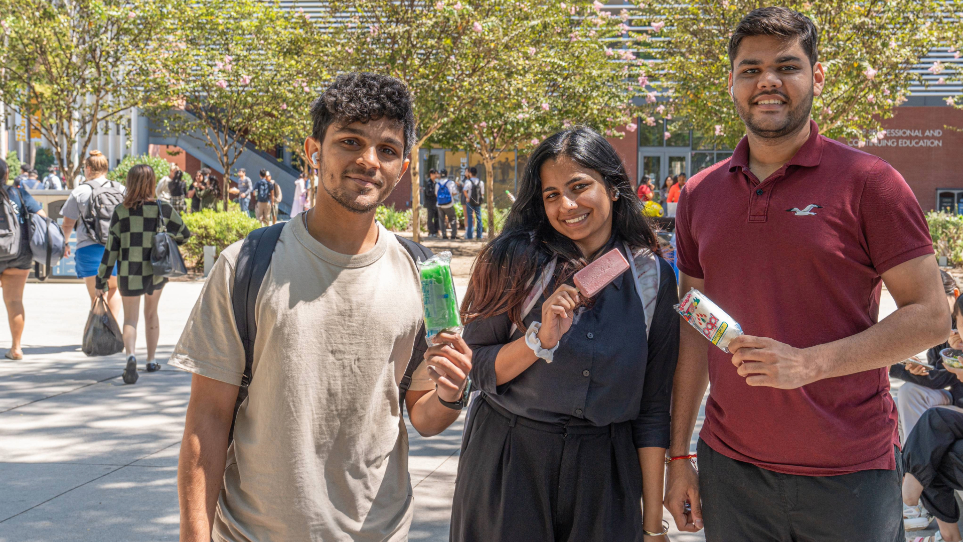 Three students smile while eating popsicles. 