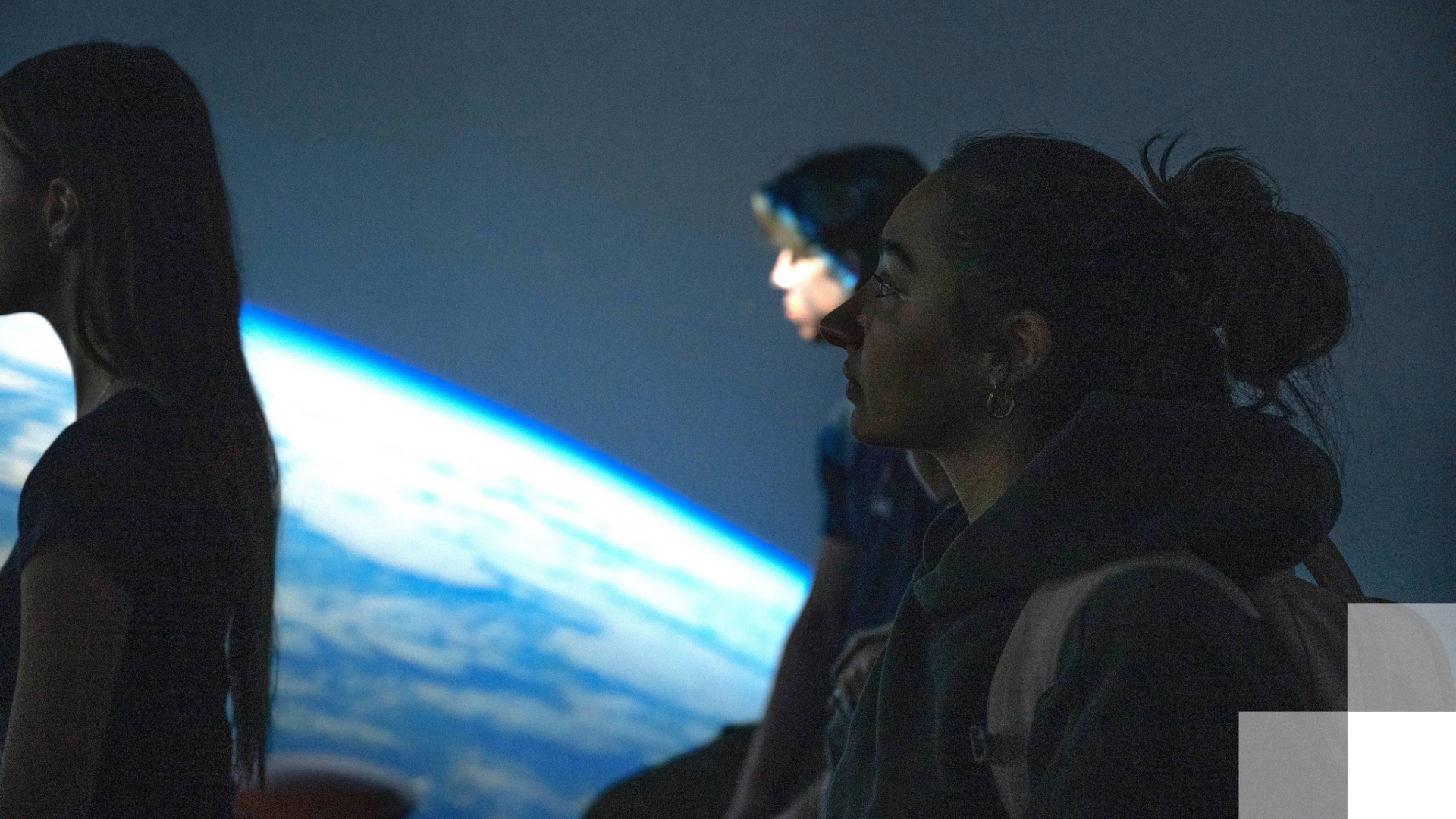 Girl stands in front of giant screen showing an image of the world. 