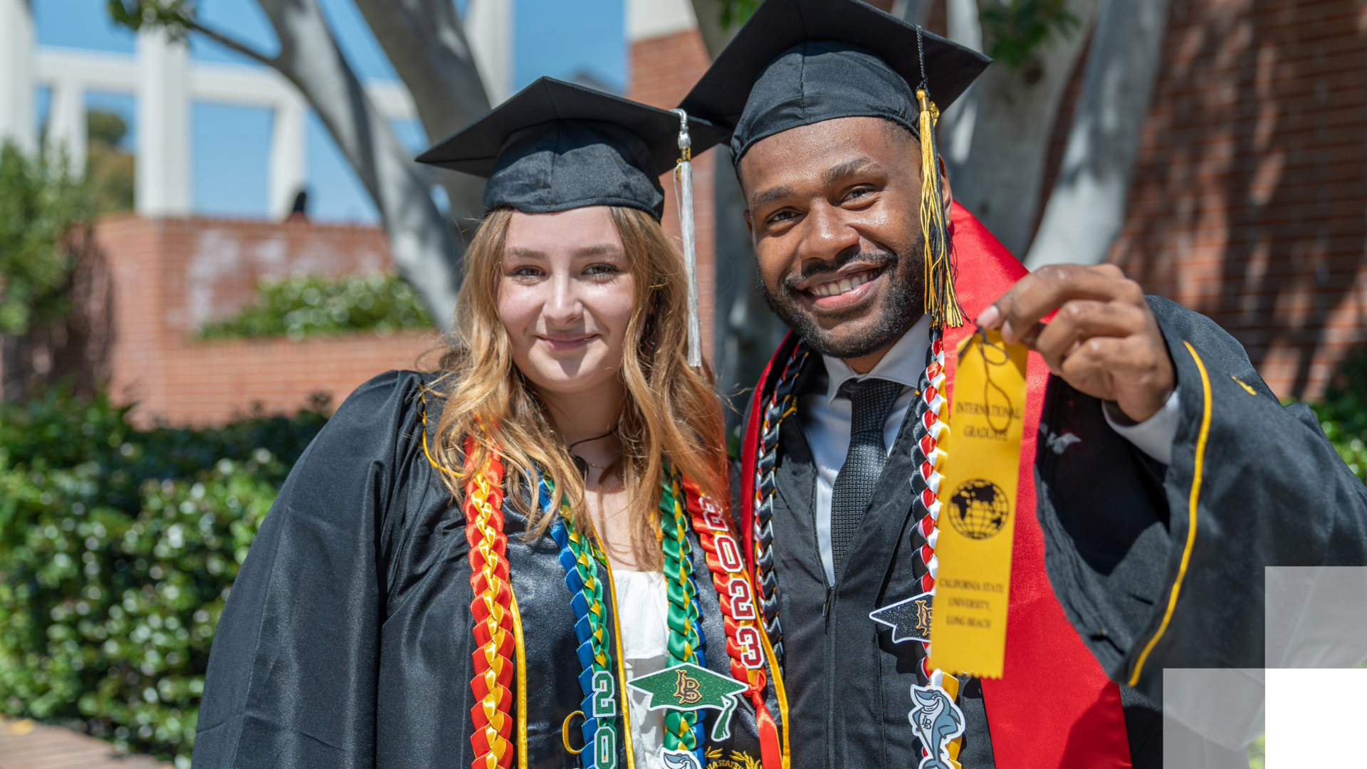 Two students in graduation robes smile at camera.