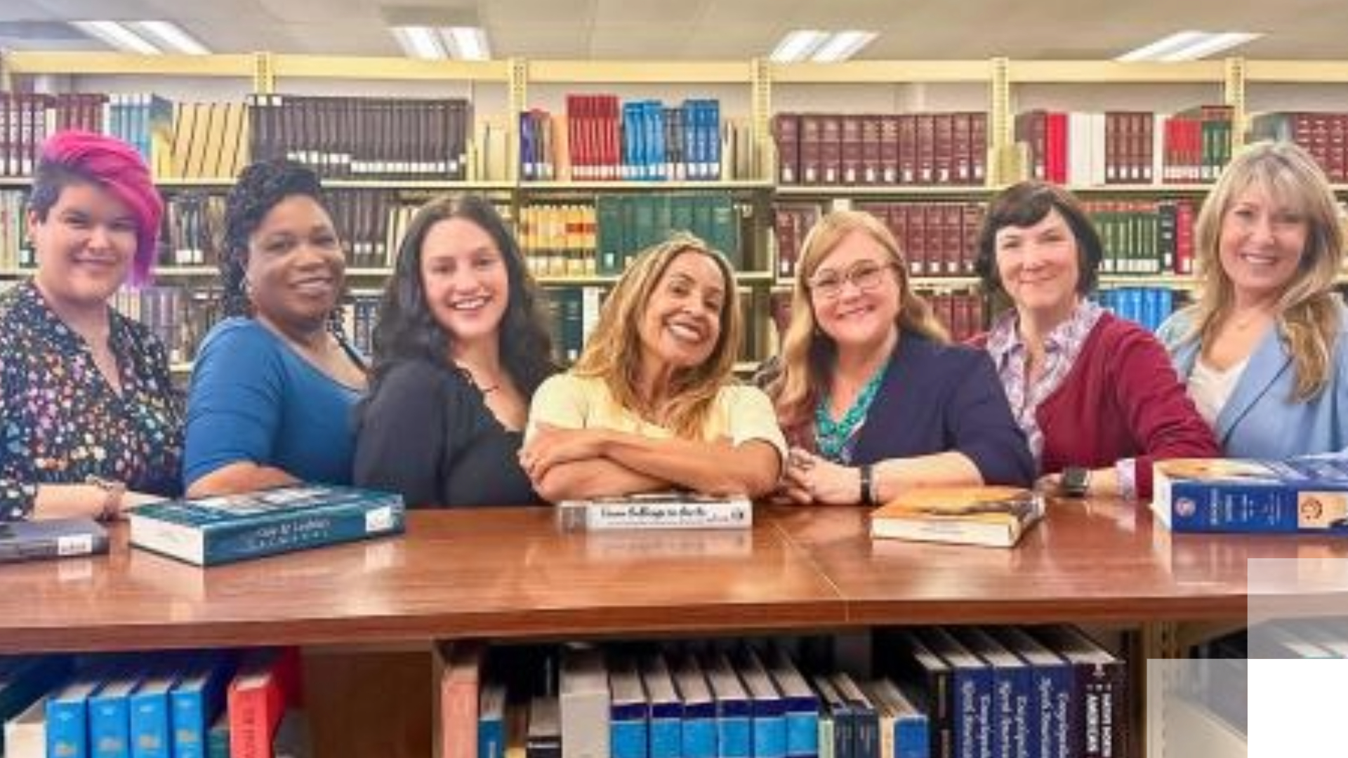 Women smile in front of book case. 