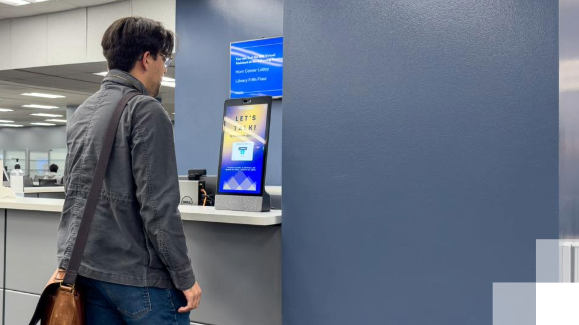 A student stands in front of a virtual assistant tablet. 