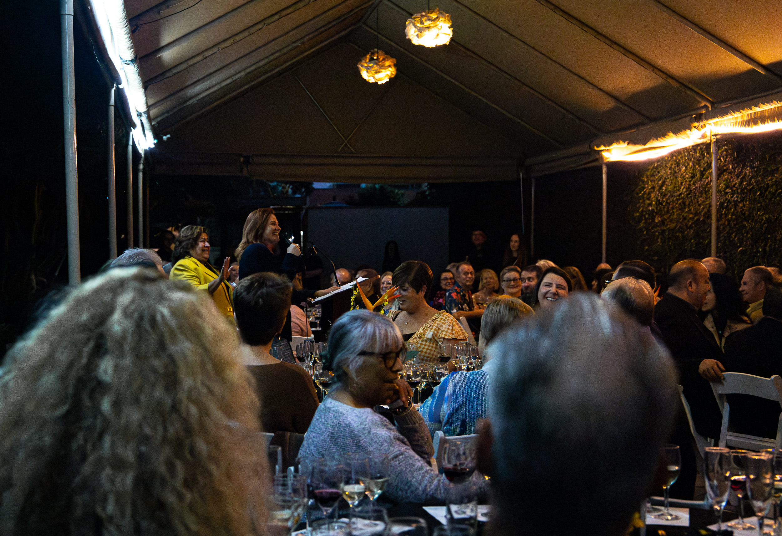 Speakers in a tented room with tables full of people