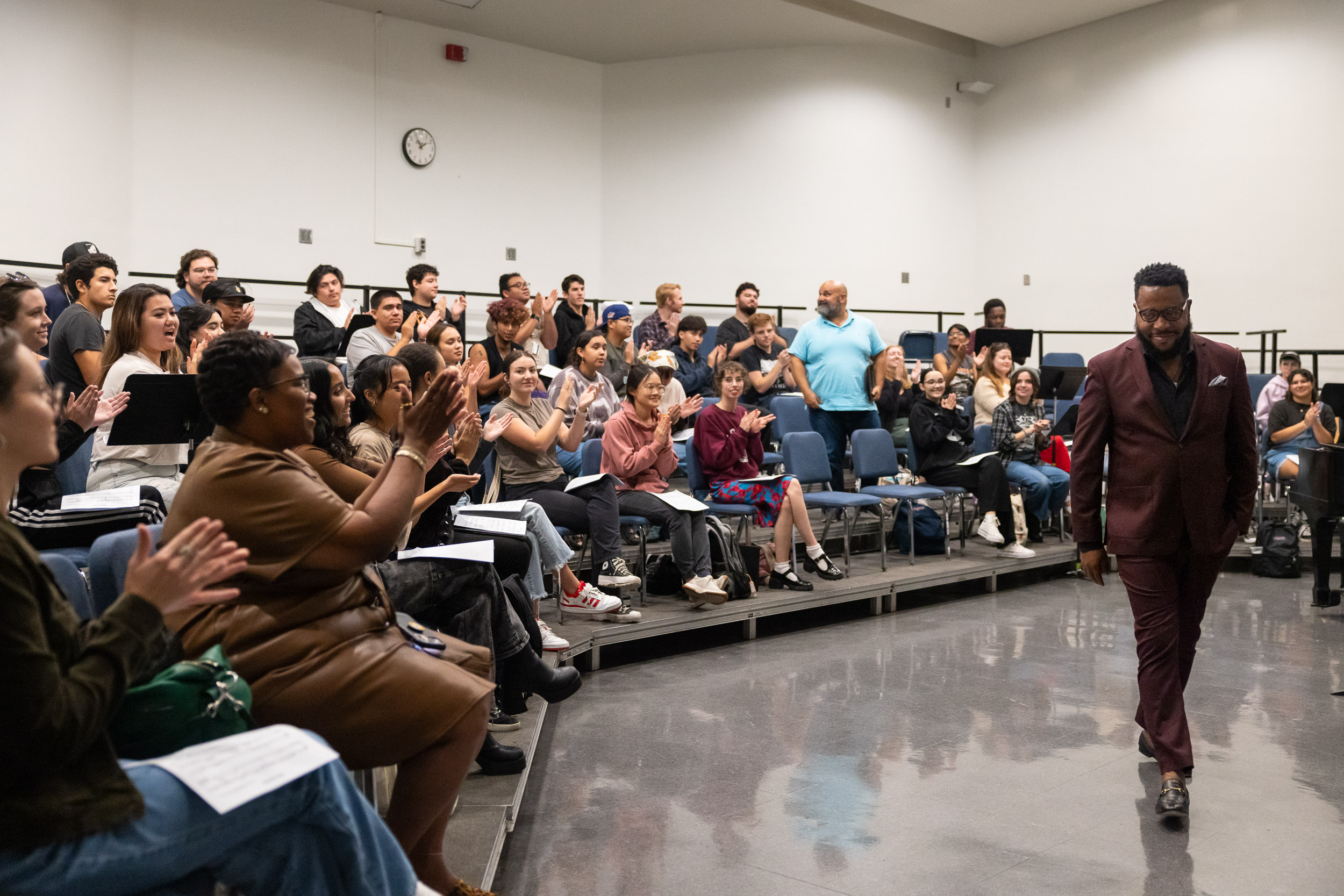 Guest musician Ananias Montague walks past an applauding choral class in a rehearsal room.