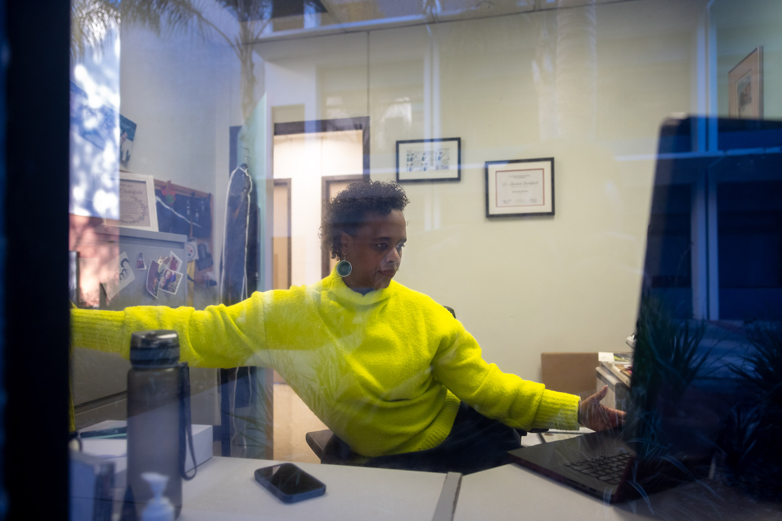 Professor Rashida Crutchfield at her desk, as seen through a window