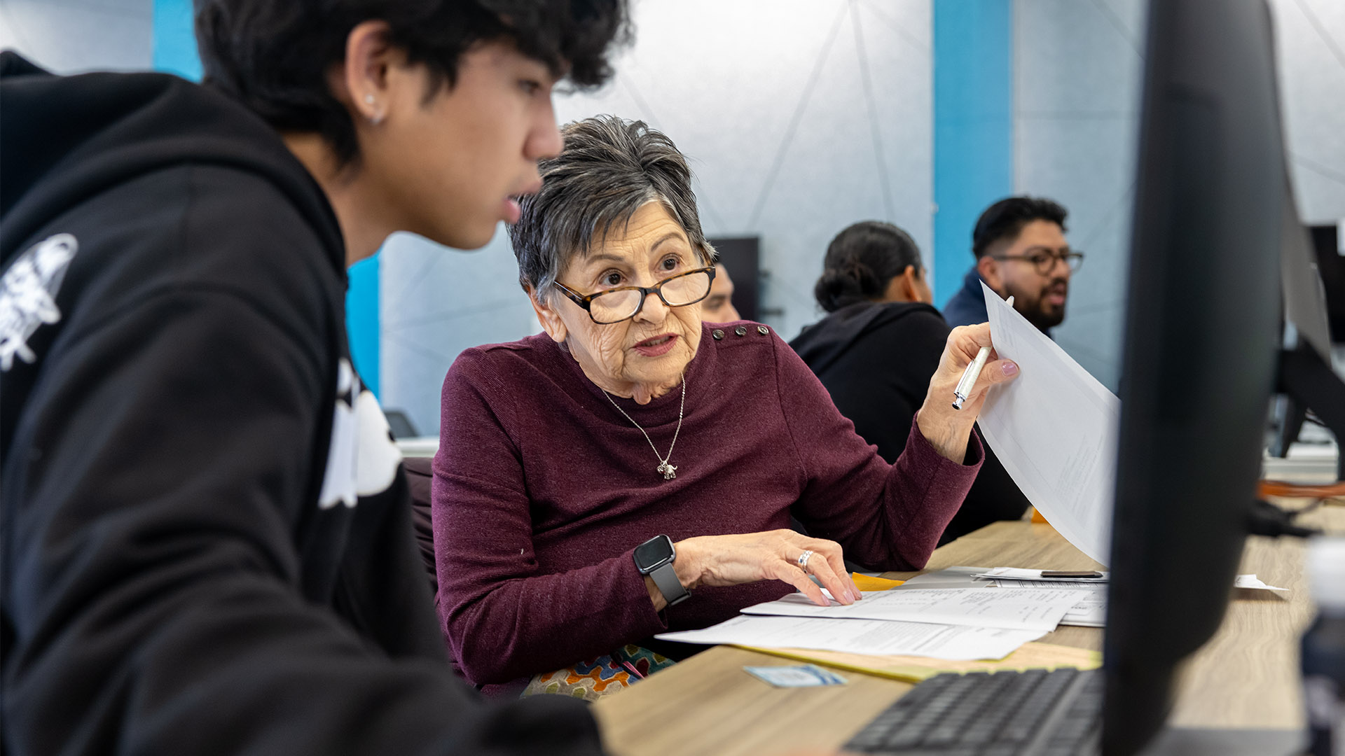 An older woman in glasses discusses her tax documents with accounting student in the VITA lab.