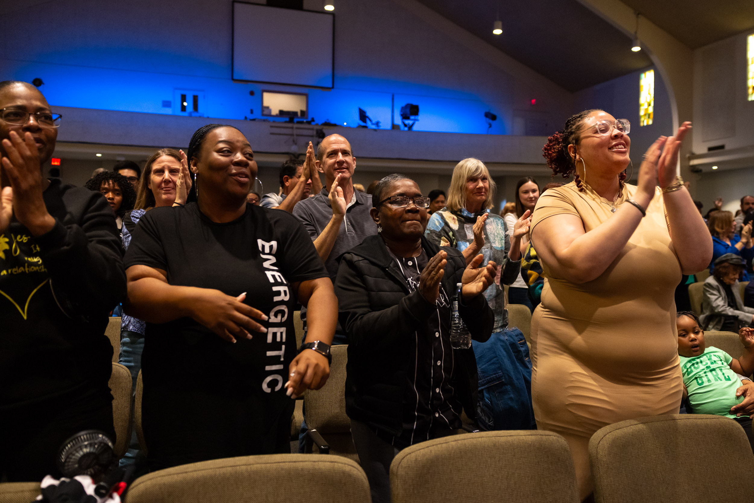 Audience members stand and clap, smiling and engaged in the Community Gospel Choir Concert