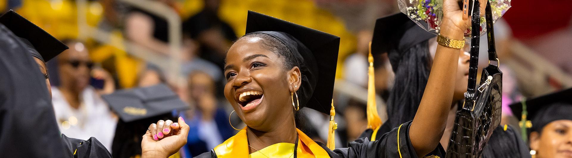 Black graduate in a cap and gown cheering on her graduation day amongst the crowd