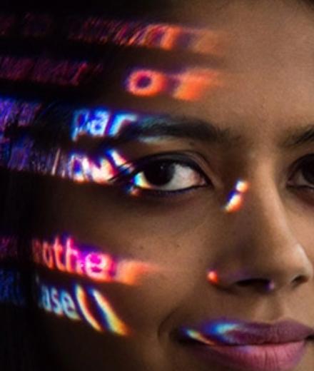 A woman with code illuminated on her face smiles at the camera. 