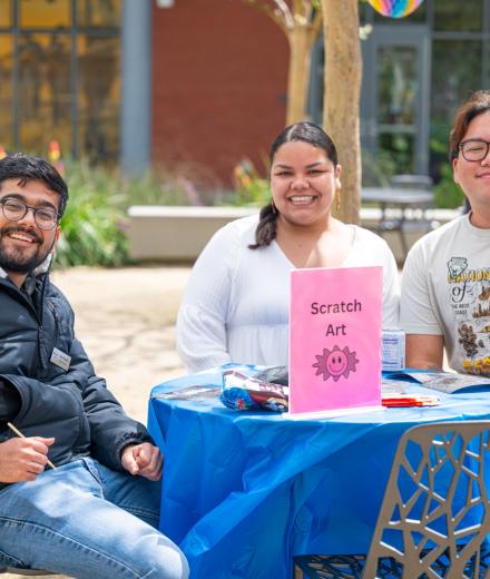 Three people seated at a scratch art activity table.