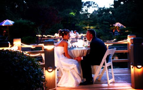 The bride and group speak to each other at their table on the koi deck of the garden.
