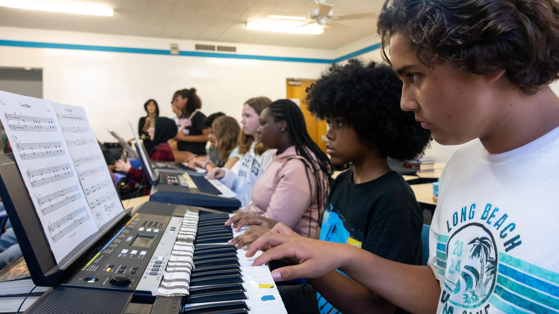 A line of children playing electronic keyboards during music practice