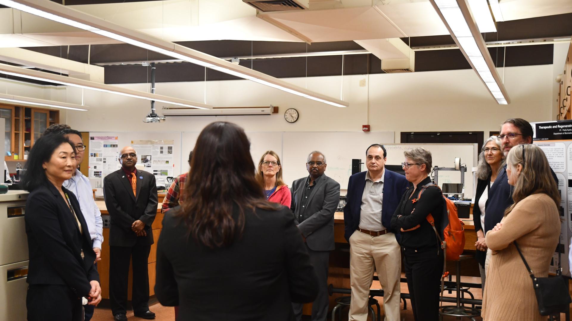 College of Engineering Deans huddled together listening to a faculty member talk about their instructional lab