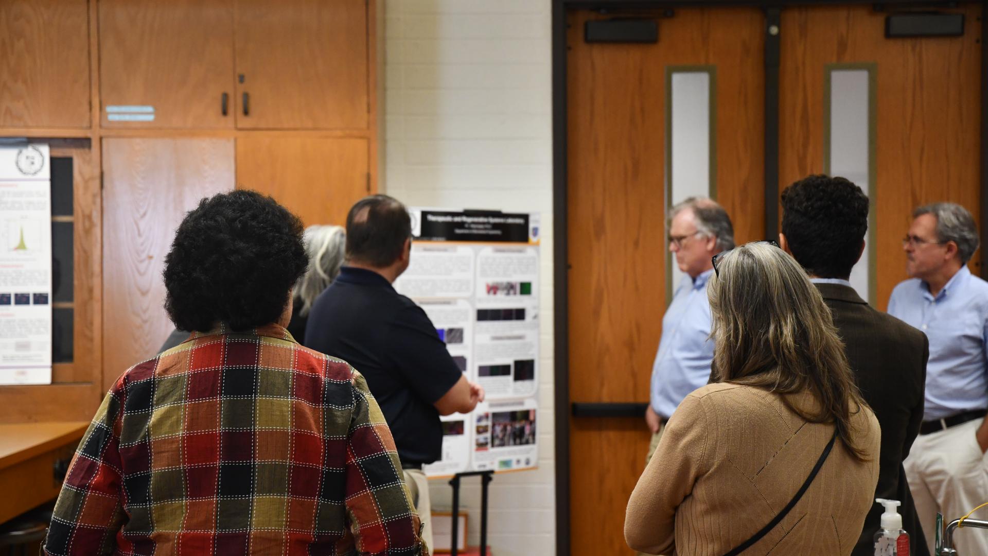 Several College of Engineering Deans looking at a poster board with research displayed on it