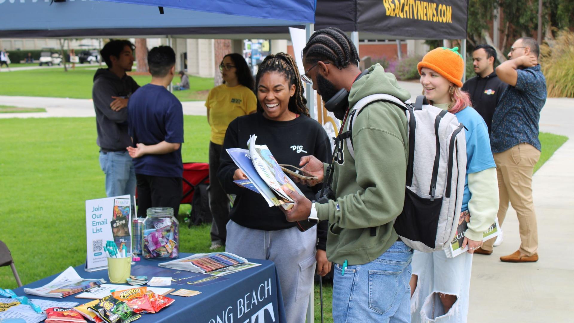 Two students smiling and grabbing fliers from an outreach table at CLA Day!