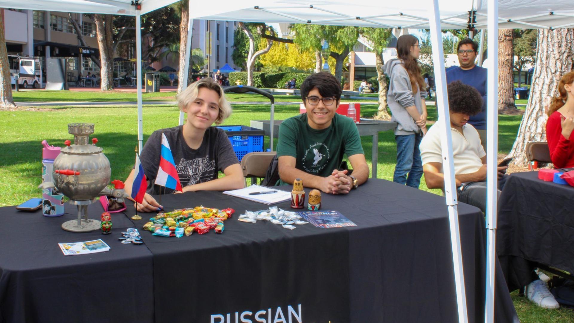 two students sitting at the Russian Languages outreach table with fliers and materials