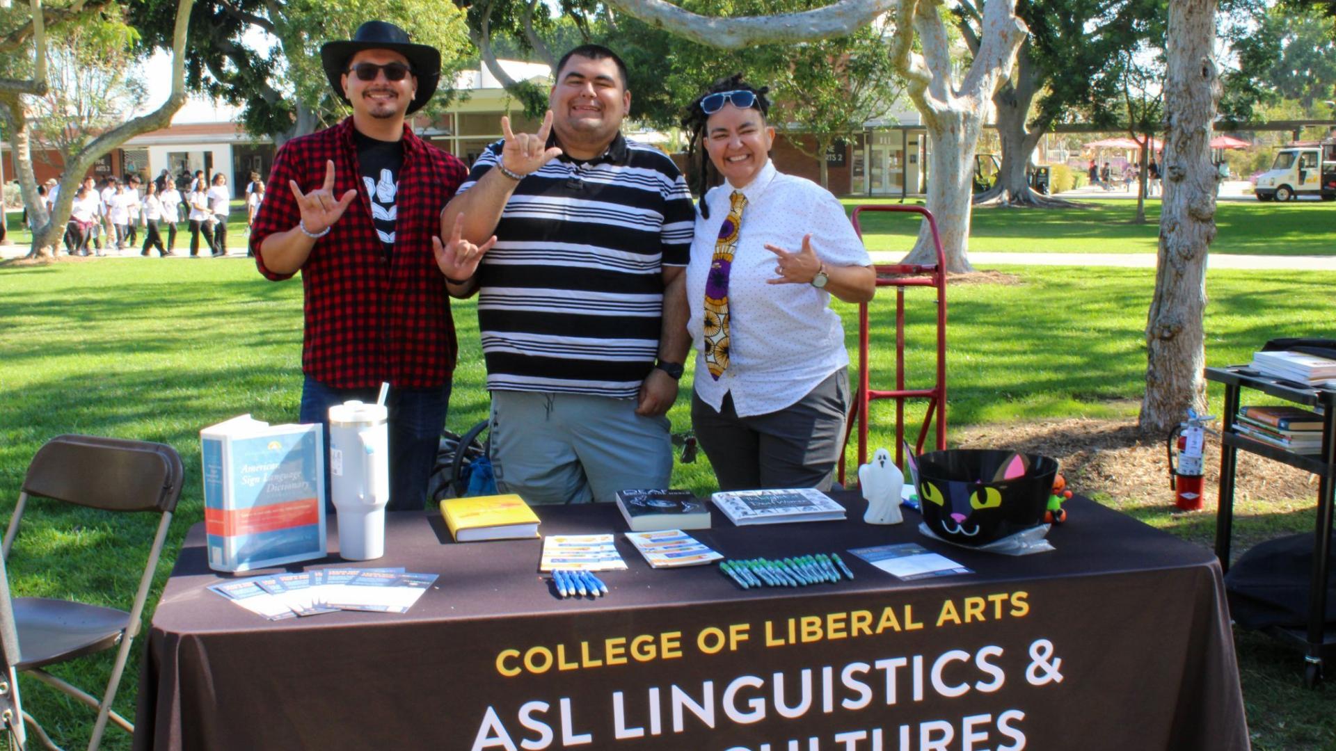 Three staff members signing by the ASL linguistics and deaf cultures outreach table