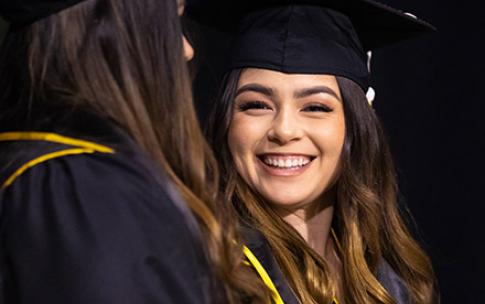 Hispanic female grad smiles at another student