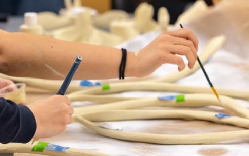 Students use brushes to paint 3D-printed rib bones of a humpback whale, spread out on a table.