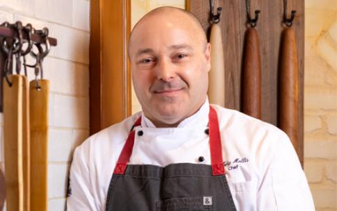 Disneyland chef Toby Hollis stands against a brick wall with wooden utensils hanging beside him.