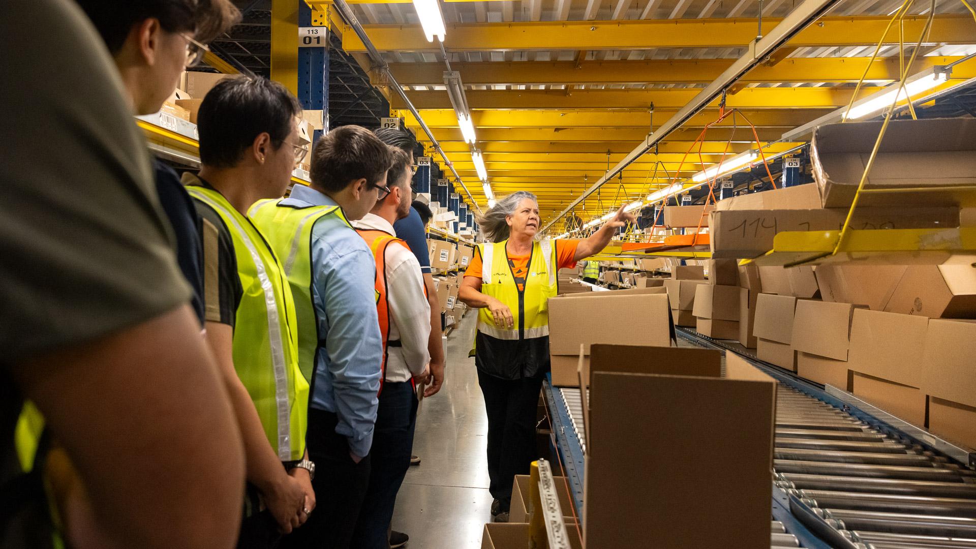 A tour guide speaking to students watching boxes move along an industrial conveyor