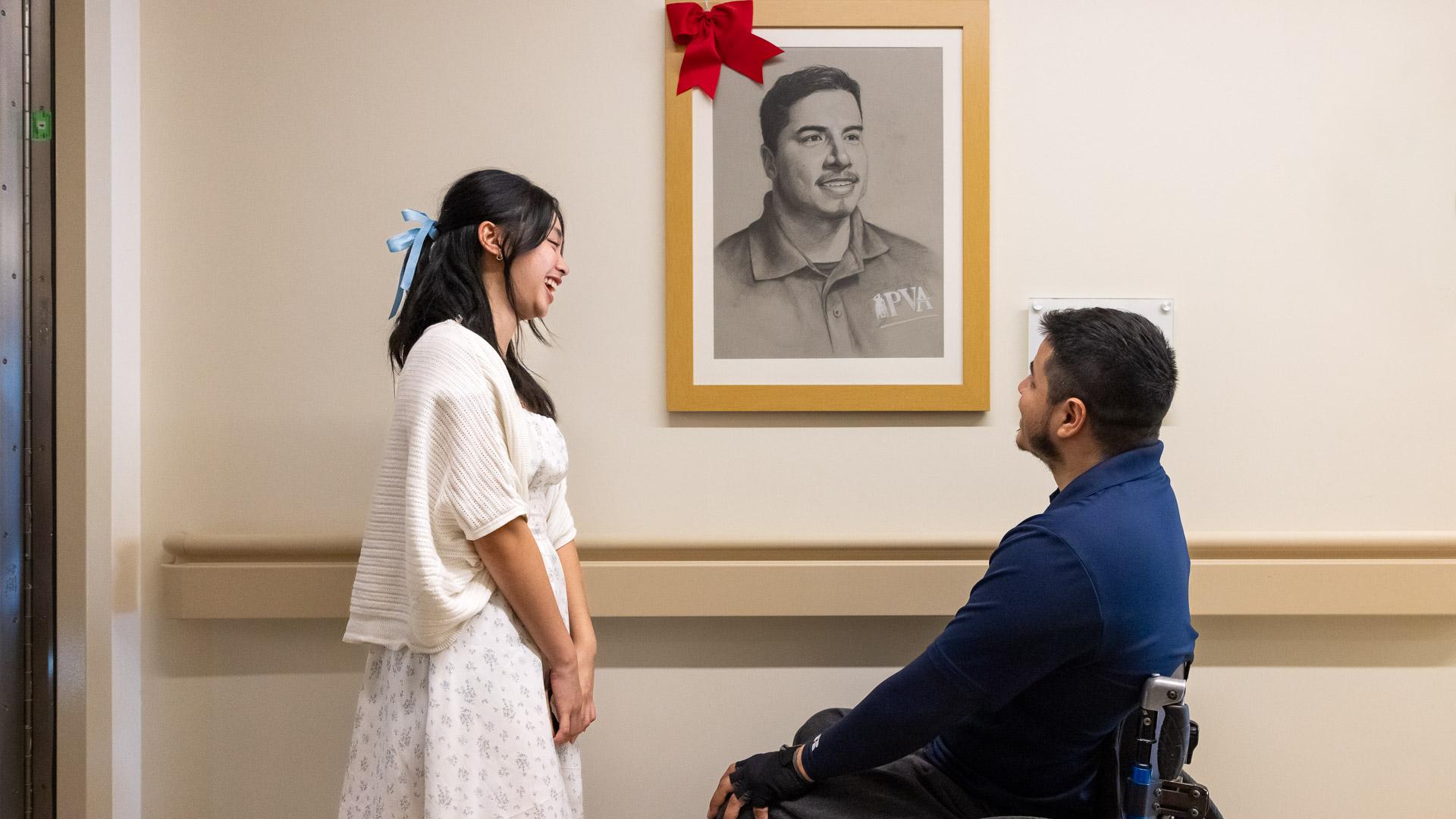 Carina Tan, left, and Jose Reynoso in front of veteran's portrait