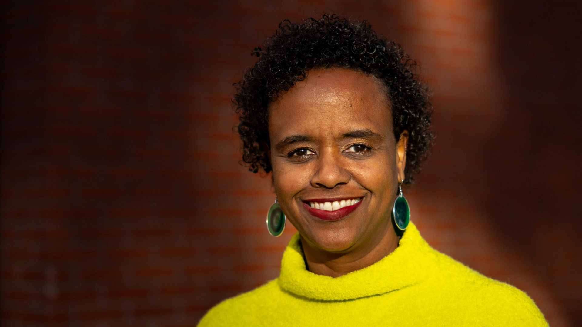 Professor Rashida Crutchfield smiling and wearing a yellow sweater.