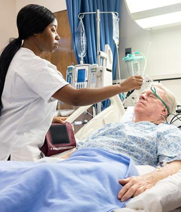 A student nurse at CSULB checks on a mock patient in a hospital bed at the school.