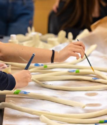 Students use brushes to paint 3D-printed rib bones of a humpback whale, spread out on a table.